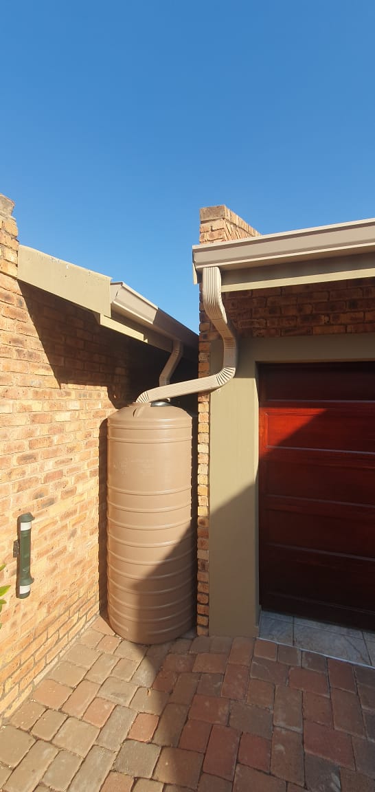 Downpipe feeding a rainwater harvesting tank beside a brick wall
